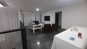 Ein modernes Wohnzimmer mit einer Couch, Sesseln, einem Fernseher und einem Tisch mit Gegenständen darauf.