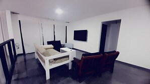 Ein modernes Wohnzimmer mit einer Couch, einem kleinen Tisch, einem an der Wand montierten Fernseher und einem dunklen Boden.