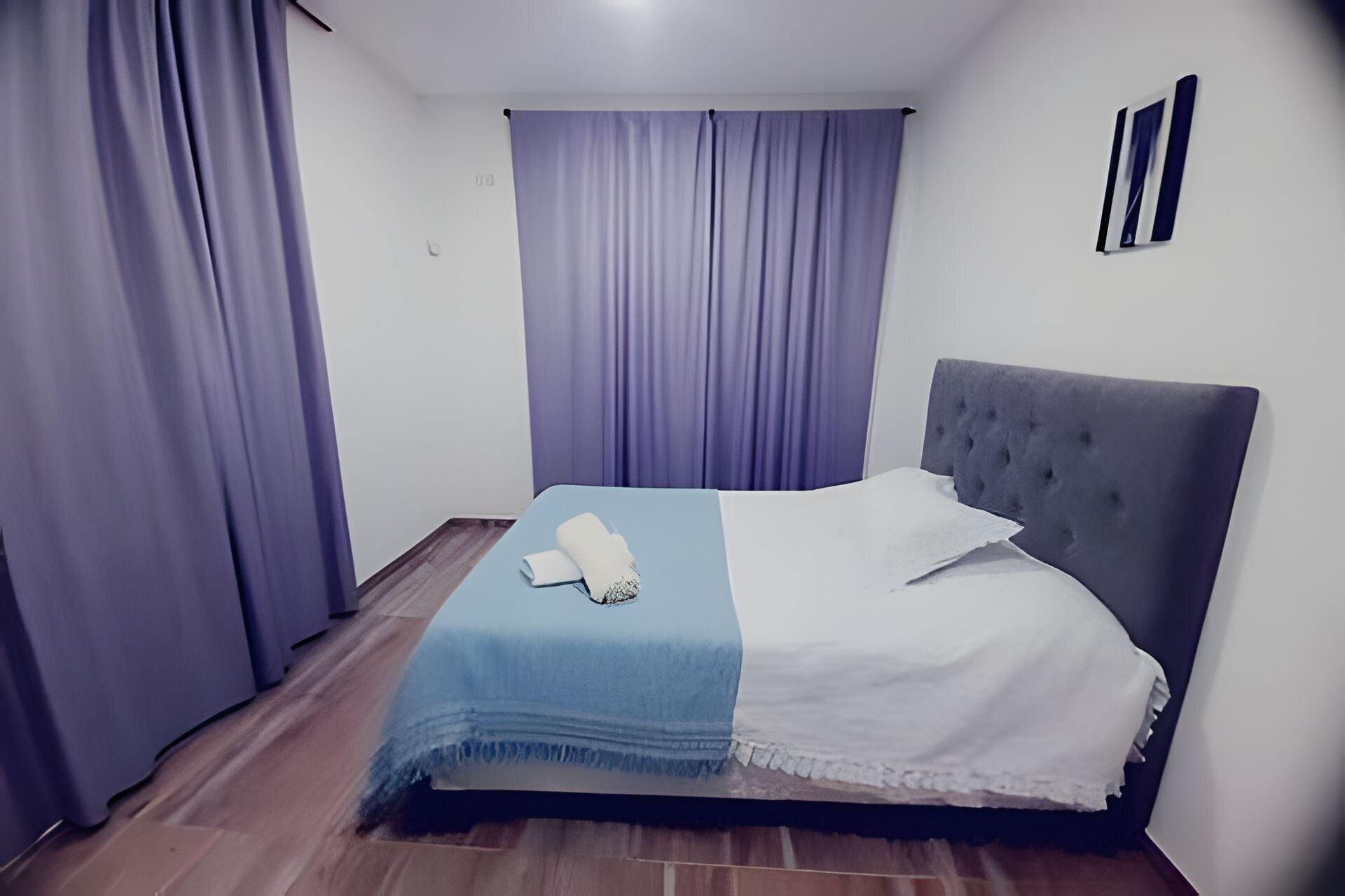 Une chambre à coucher avec un lit, une couvre-lit bleue et blanche, et des rideaux violets.