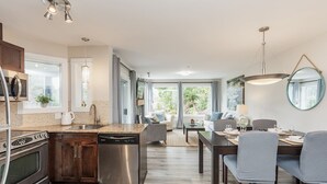 Una cocina moderna con electrodomésticos de acero inoxidable, un comedor con mesa y sillas, y una sala de estar con sofá y televisor.