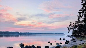 Vista de un lago con agua tranquila, rocas y una orilla bordeada de bosque.