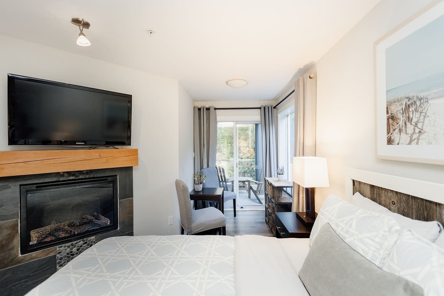 A hotel room with a bed, a TV, a fireplace, a dining area, and a balcony.