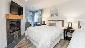 Een hotelkamer met een open haard, een bed met witte beddengoed, een aan de muur bevestigde televisie en een raam met uitzicht op bomen.