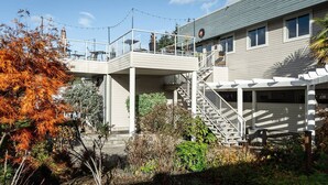 Een gebouw met twee verdiepingen, een overdekt terras, een trap en een tuin met herfstkleuren.