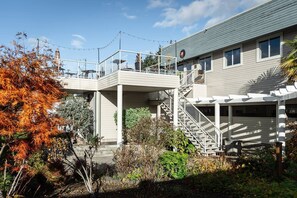 Un edificio de dos plantas con un espacio exterior cubierto, una escalera y un jardín con follaje otoñal.