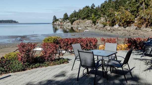 Een terras met buitenmeubilair met uitzicht op een meer, omgeven door bomen en struiken.