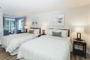 A hotel room with two beds, a desk, and chairs.