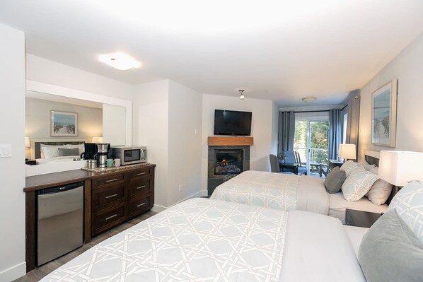 A hotel room with a bed, a desk with a microwave, a television, a fireplace, and a balcony with a view.