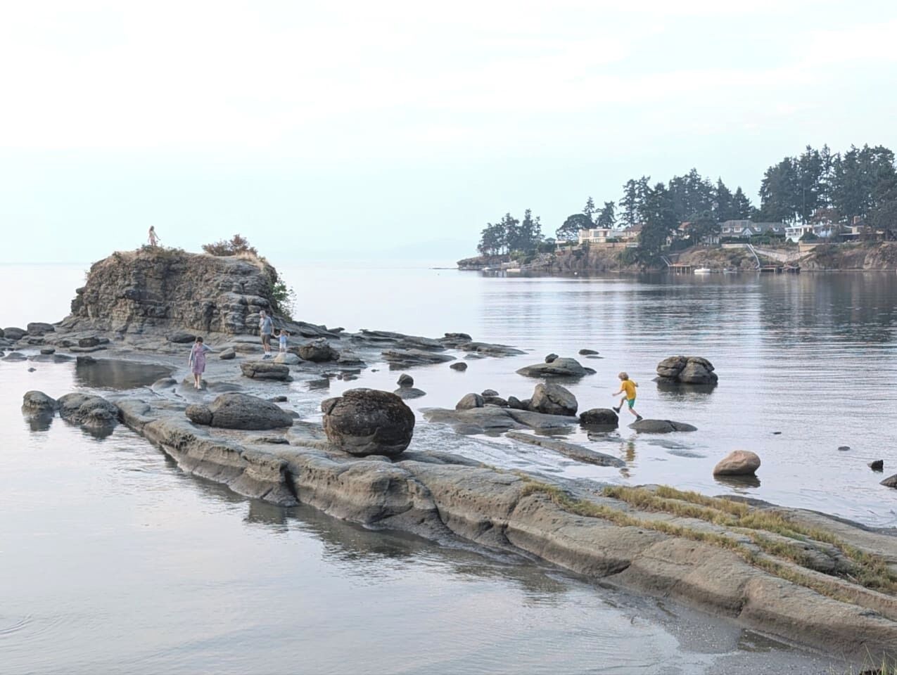 A rocky shoreline with people walking on rocks and a small island with a structure.