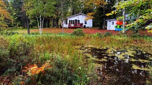 Eine Hütte, umgeben von einem Teich mit Seggen, mit einer roten Terrasse und einem kleinen Schuppen voller bunter Kanus.