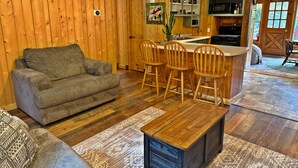 Ein gemütliches Wohnzimmer mit einer Couch, Holzstühlen, einem Couchtisch und einer Küchenzeile mit Spüle und Schränken.