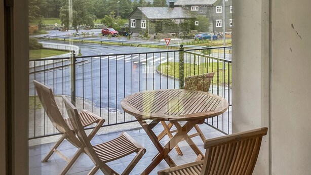 Un balcon donnant sur une route, une table ronde en bois et deux chaises en bois.