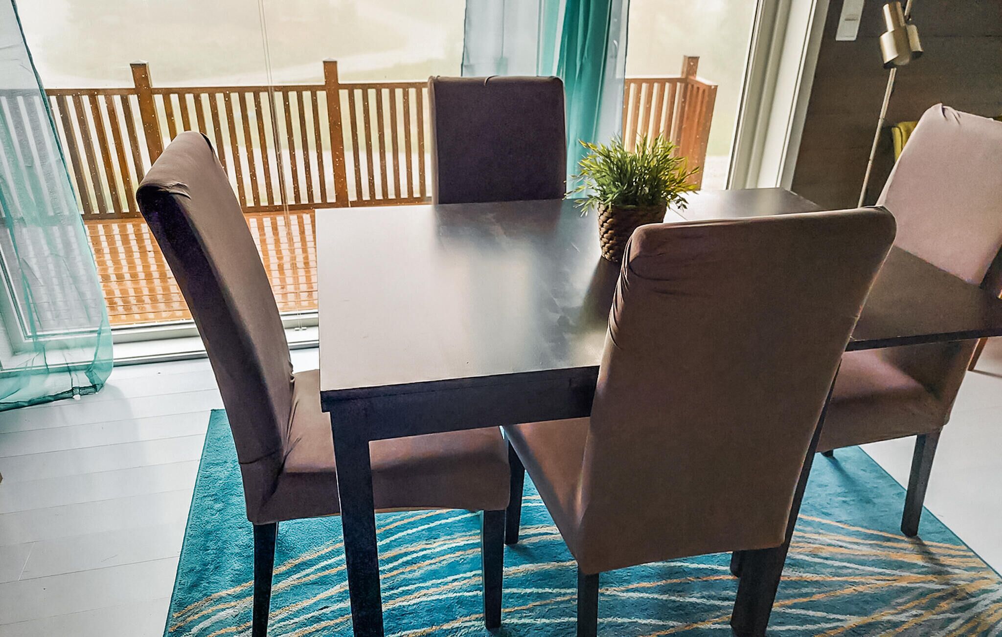 Un coin repas avec une table et quatre chaises, une petite plante posée sur la table et, par la fenêtre, une vue sur une clôture en bois.