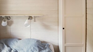 Quarto com cama, parede branca, estante de madeira com duas luminárias e uma porta.