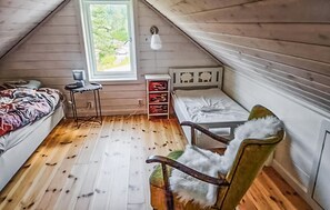 Ett litet, mysigt sovrum på vinden med träväggar och ett sluttande tak. Rummet innehåller en säng, en stol, ett litet bord och ett fönster med utsikt över grönskan utanför.