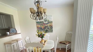 Un comedor con una mesa y sillas blancas, una araña y un cuadro en la pared.