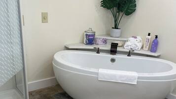 Une salle de bain avec une baignoire sur pieds, une douche à parois de verre, une plante en pot et des articles de toilette rangés sur une étagère.