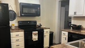 Una cocina con estufa negra, armarios blancos, microondas y encimera de granito.