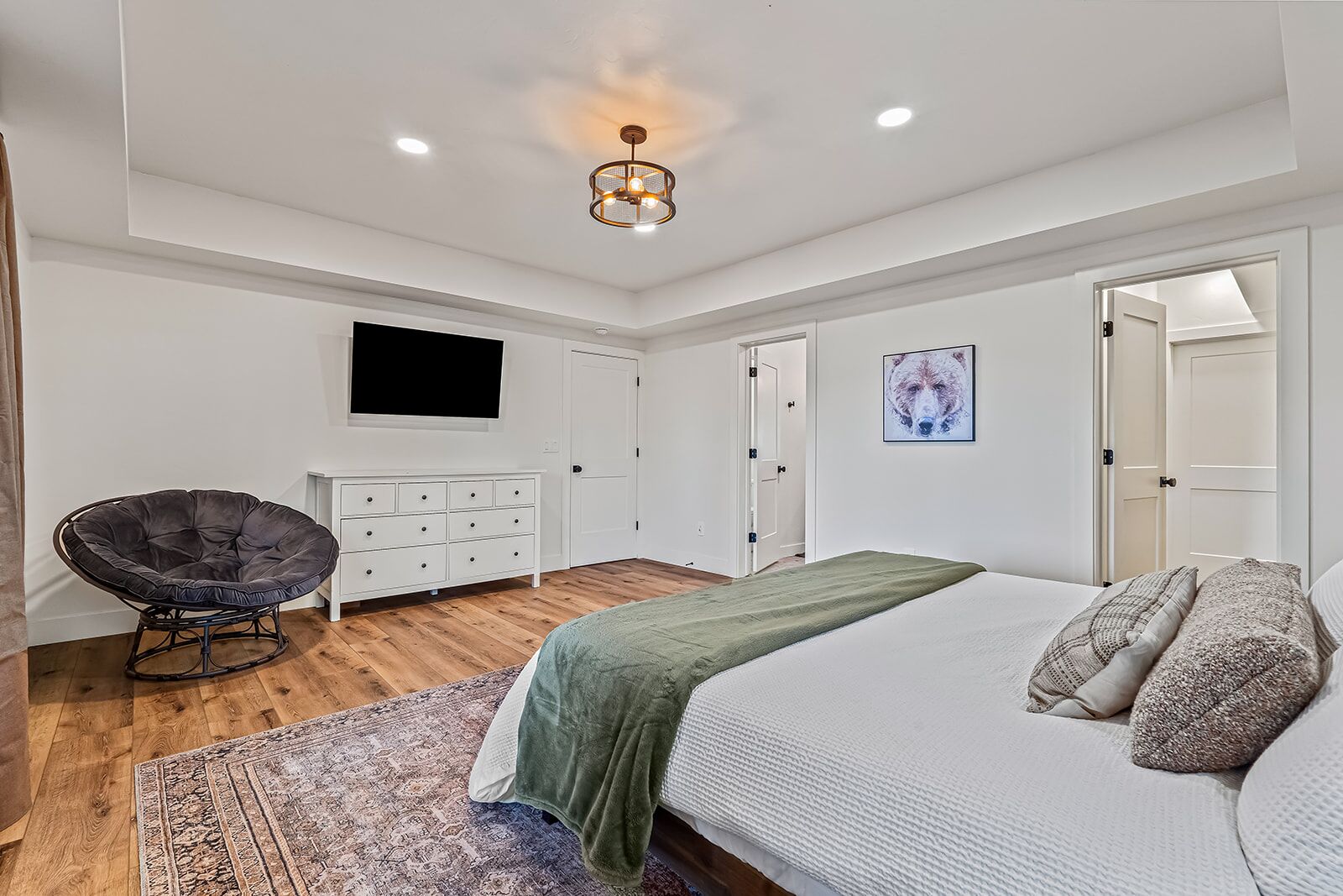 Un dormitorio con una cama, una silla, un tocador, un televisor y una puerta.