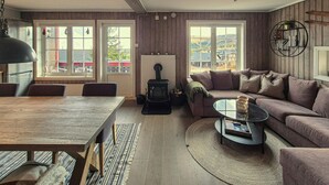 Uma sala de estar acolhedora com uma mesa de madeira, um sofá e uma mesa de centro de vidro. Há uma lareira e uma janela com vista para o exterior.