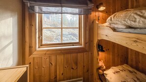 Una habitación de cabaña de madera con literas, una ventana con vistas a árboles y una lámpara en la pared.