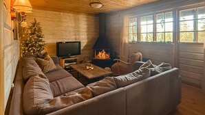 Interior acogedor de una cabaña con techo de madera, chimenea, televisor y un árbol de Navidad.