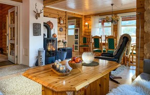A cozy log cabin interior with a central wooden table, a fireplace, and a dining area with green upholstered chairs. - Pet friendly home in Lesjaskog with WiFi (Lesjaskog)