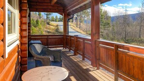 A wooden deck with wicker furniture and a marble table, overlooking a mountainous landscape.