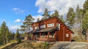 A log cabin with a porch, surrounded by trees and a clear sky.