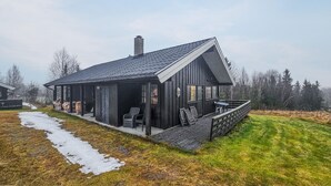 En enkel stuga med en veranda, en skorsten och en liten terrass.