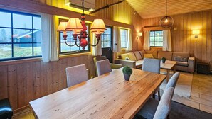 En mysig stuga med en inredning som inkluderar ett matbord i trä, stolar, en soffa och en hängande lampa.