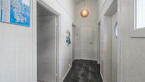 Un corridoio con pavimento in legno scuro, pareti bianche e un lampadario.