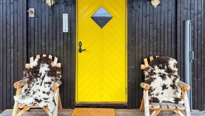A yellow door with a diamond-shaped window, flanked by two rustic wooden chairs with fur throws. - Stunning home in Røros with sauna (Røros)
