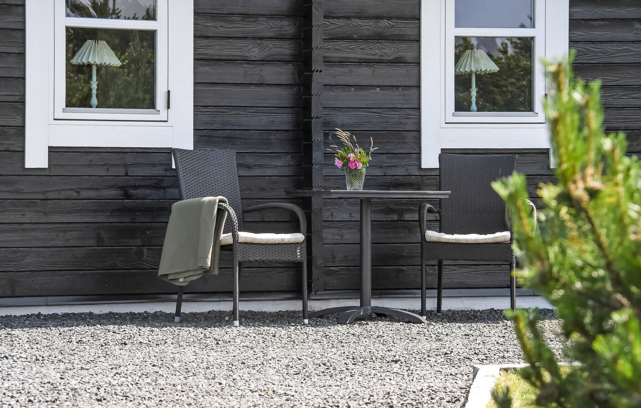 A wooden cabin with two chairs and a table, a window with a lamp, and a small potted plant on the table.