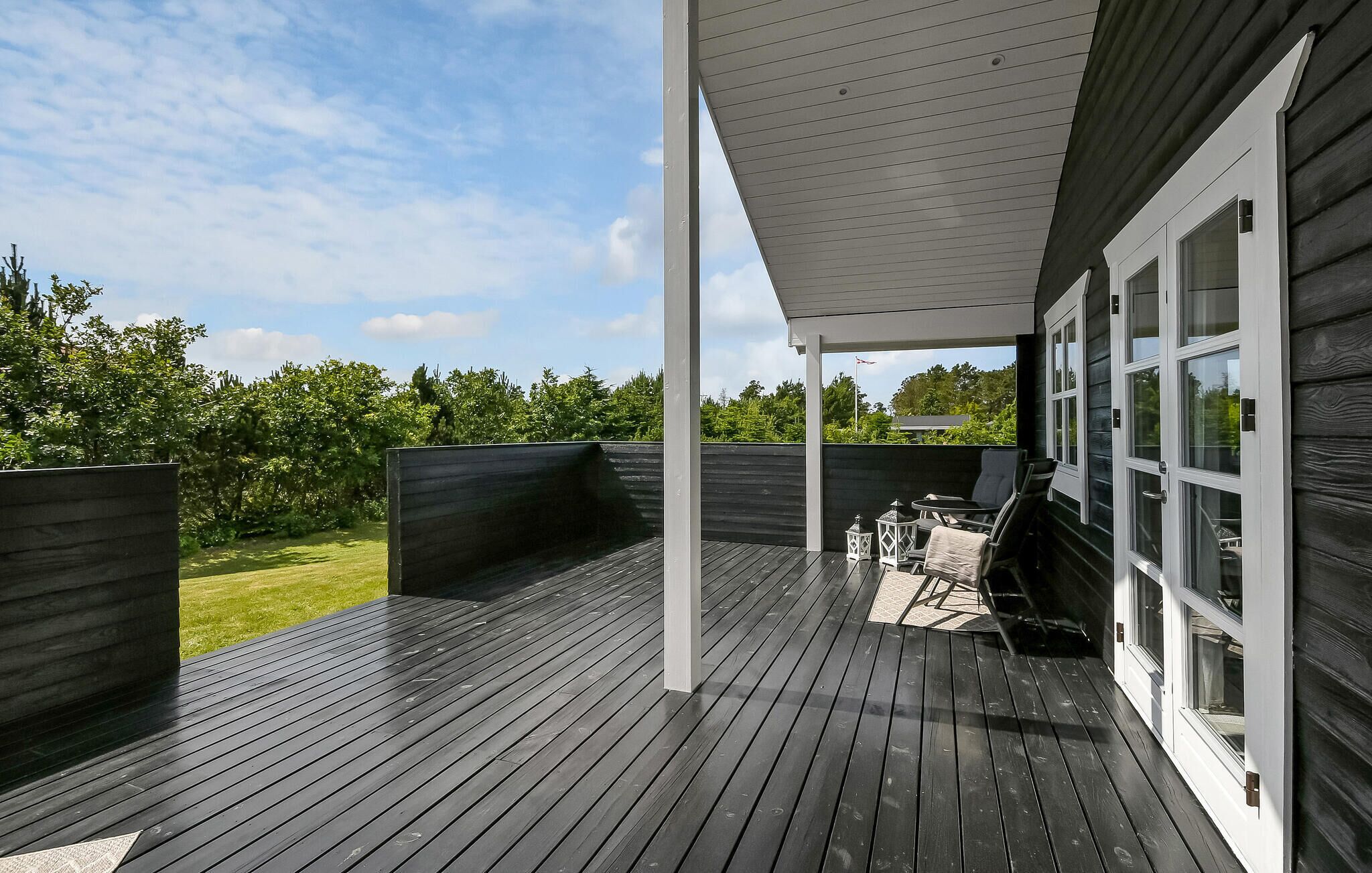 Eine überdachte Terrasse mit Tisch und Stühlen, ein Holzzaun und Blick auf eine grüne Landschaft.