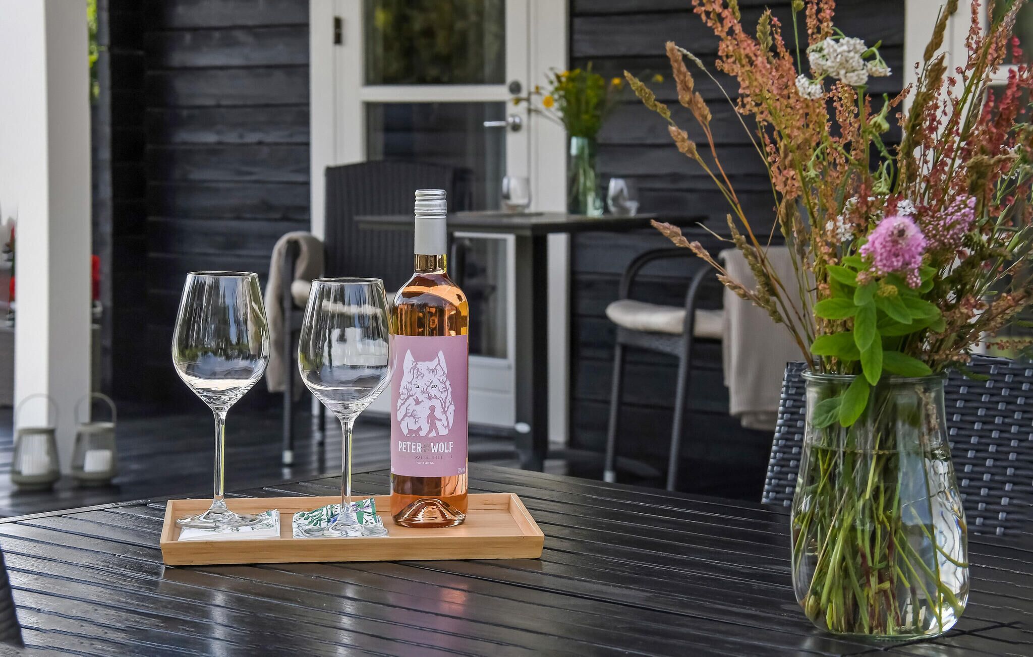 A bottle of wine, two glasses, and a vase with flowers on a table.