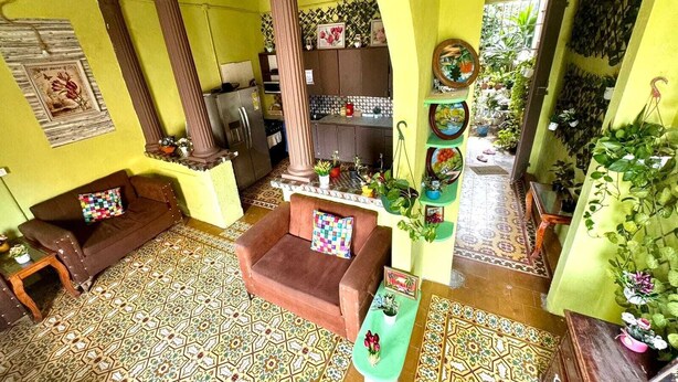 A brightly colored living room with patterned floor tiles, a sofa, a coffee table, and a kitchen area with a refrigerator and cabinets. - LA ESPAÑOLA GUESTHOUSE 1 (Santo Domingo)