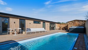 Ein Schwimmbad mit Holzterrasse, Liegestühlen und Whirlpool.