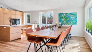 Eine moderne Küche mit Holdekor-Schränken, ein Essbereich mit einem langen Holztisch und Stühlen sowie ein großes abstraktes Bild an der Wand.