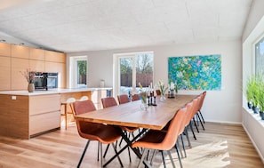 A modern kitchen with wooden cabinets, a dining area with a long wooden table and chairs, and a large abstract painting on the wall. - Beautiful home in Ejstrupholm (Ejstrupholm)