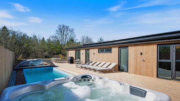 Ein moderner Poolbereich im Freien mit Whirlpool, Liegestühlen und einer Holzterrasse.