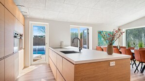 Eine moderne Küche mit Kochinsel, Essbereich mit Stühlen und Blick auf einen Garten.