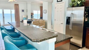 A kitchen with a central island, bar stools, a refrigerator, and a view to the outside. - 5 Star Beach Penthouse On Top Floor! Private Elevator & Extra Large Balcony (Gulf Shores)