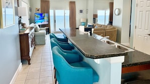 A modern kitchen with a bar area, a dining area with a view, and a living room with a sofa and a TV. - 5 Star Beach Penthouse On Top Floor! Private Elevator & Extra Large Balcony (Gulf Shores)