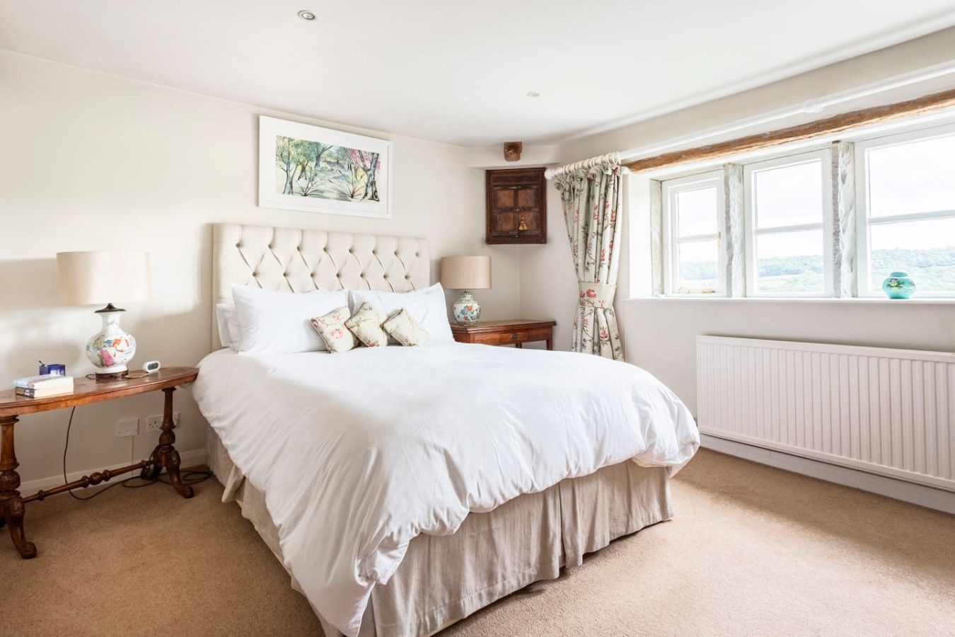 A bedroom with a large bed, two bedside tables, a window with curtains, and a radiator.