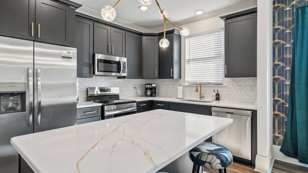 A modern kitchen with dark cabinets, stainless steel appliances, a marble island, and a unique chandelier. - The Emerald-Contemporary Art Deco–Style Townhome (Memphis)