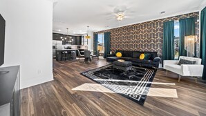 A modern living room with a dark wood floor, a black and white patterned rug, a dark sofa with cushions, a white armchair, and a ceiling fan. - The Emerald-Contemporary Art Deco–Style Townhome (Memphis)