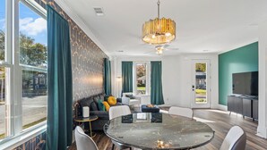 A modern dining area with a round table, white chairs, and a chandelier. - The Emerald-Contemporary Art Deco–Style Townhome (Memphis)