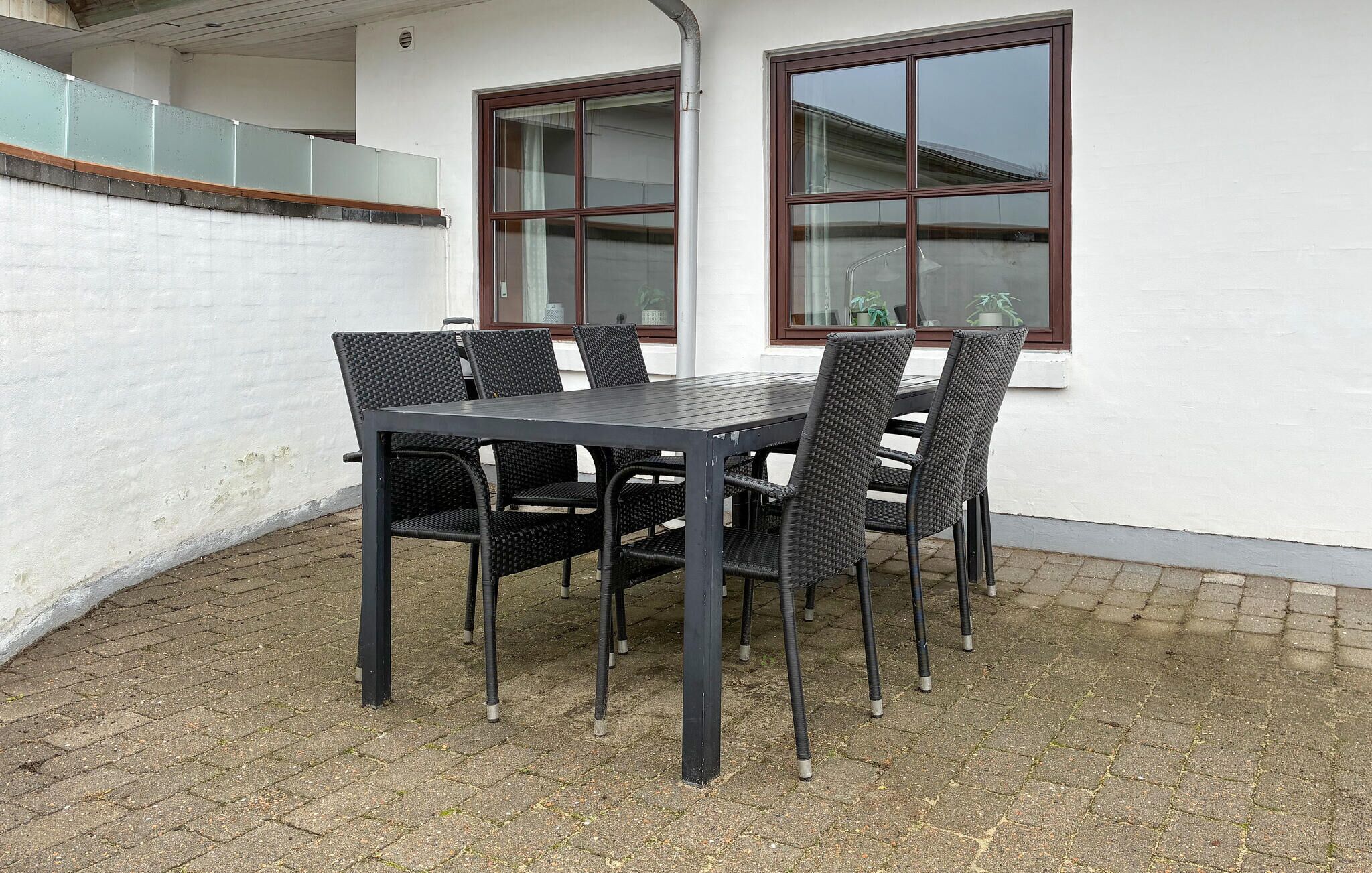 A patio with a table and chairs, a white wall, and a window with a brown frame.