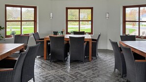 Een vergaderruimte met een lange tafel en stoelen, grote ramen met uitzicht op een groen landschap, en een betegelde vloer.